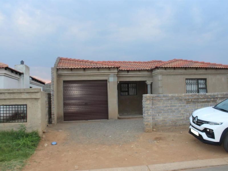 Front view of a single-story house featuring a tiled roof, integrated garage, and a gated entrance with an unpaved driveway.