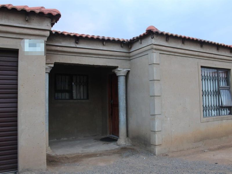 Front exterior view of a single-story house featuring a covered entrance with decorative columns, a roller garage door, and security bars on windows.