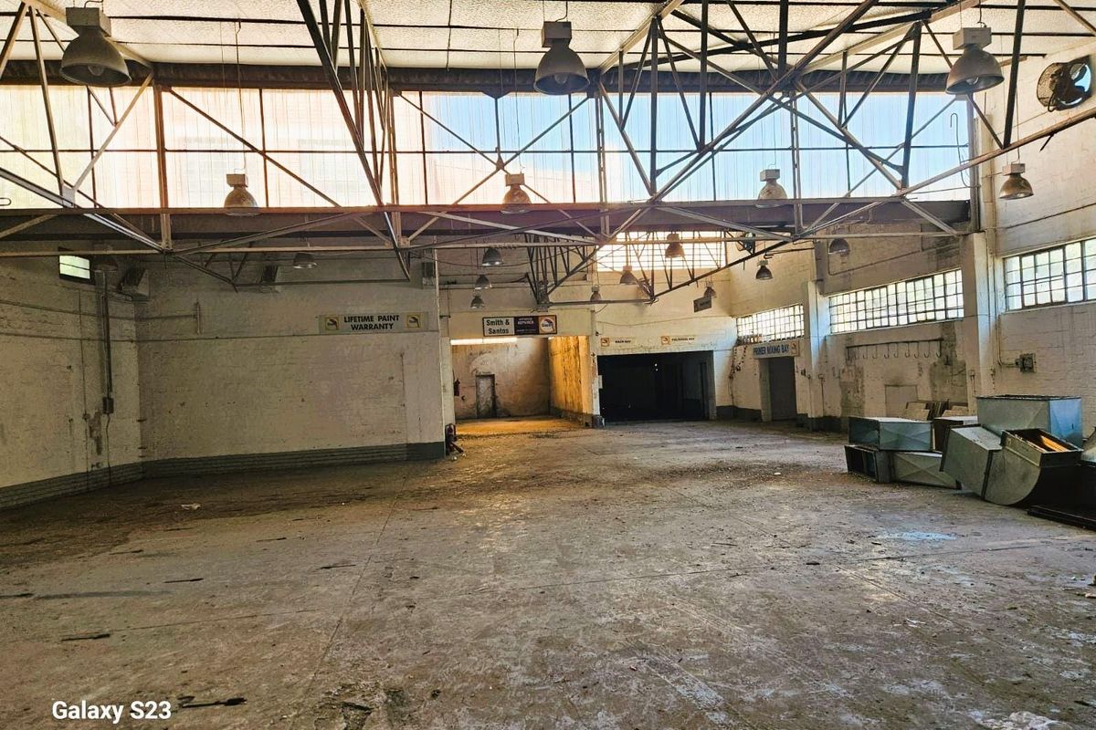 Spacious industrial warehouse interior featuring high-clearance steel truss roofing, exposed structural elements, and concrete flooring, suitable for workshop or storage use.