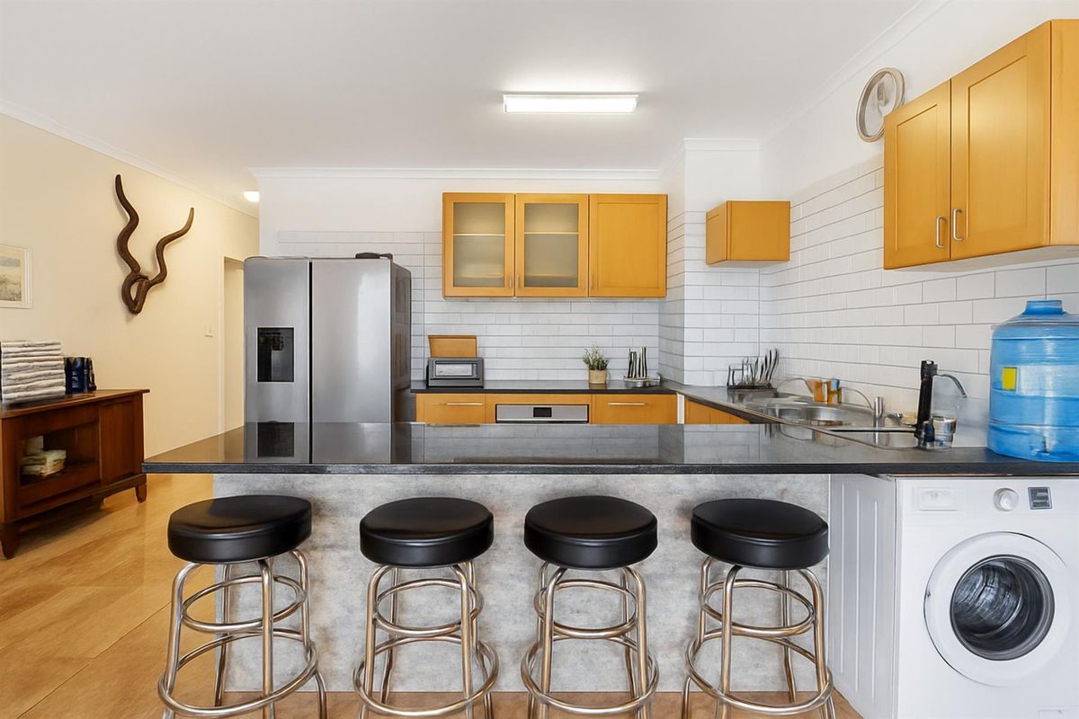 A functional kitchen featuring wooden cabinetry, a black stone breakfast bar, subway tile backsplash, and an integrated laundry space with a front-loading washing machine.