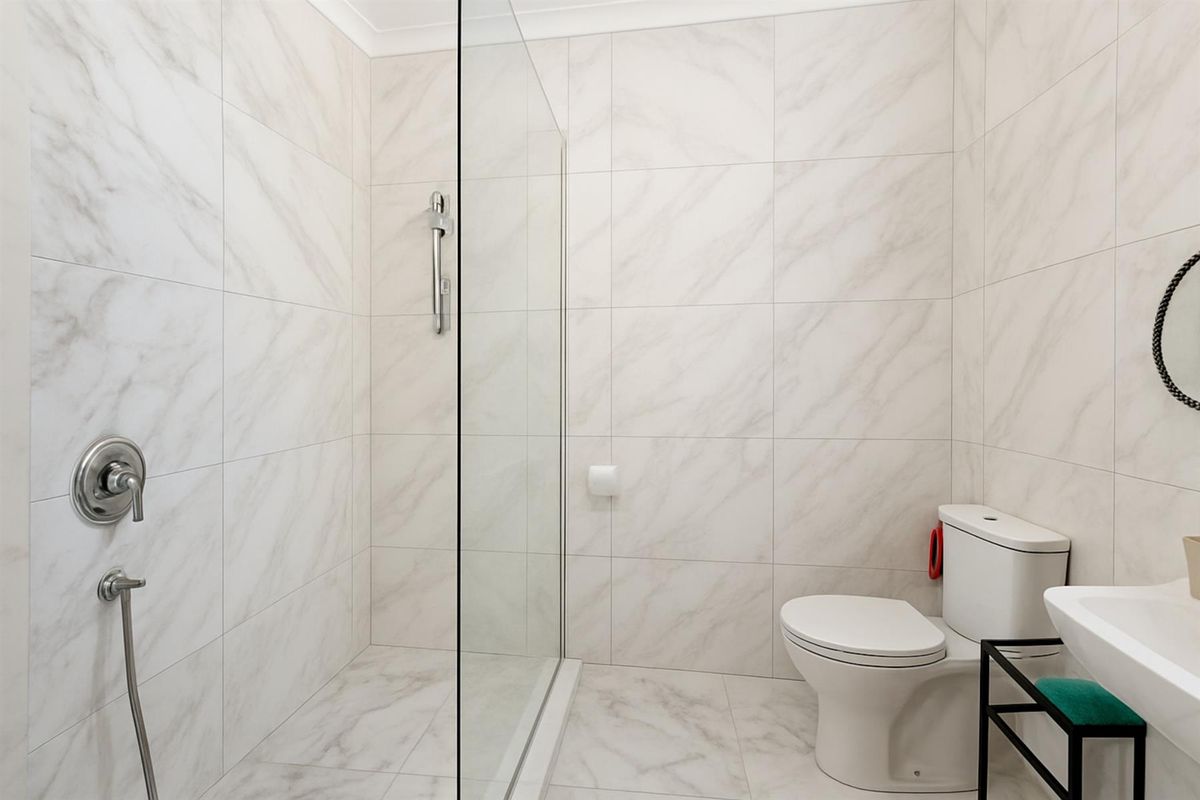 Modern bathroom featuring floor-to-ceiling marble-look tiling, a glass-enclosed walk-in shower, a wall-mounted toilet, and a sleek vanity basin.