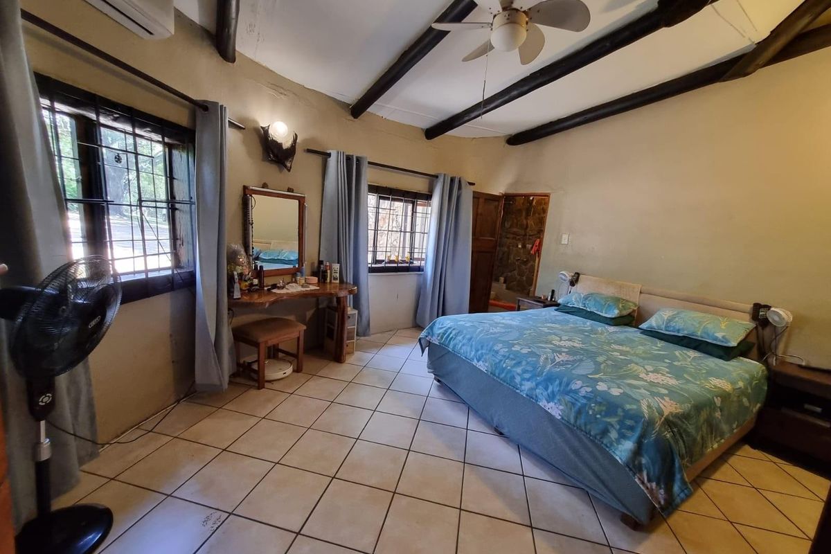 Spacious bedroom featuring exposed timber ceiling beams, tiled flooring, and large windows with security bars, offering a rustic farm-style aesthetic.