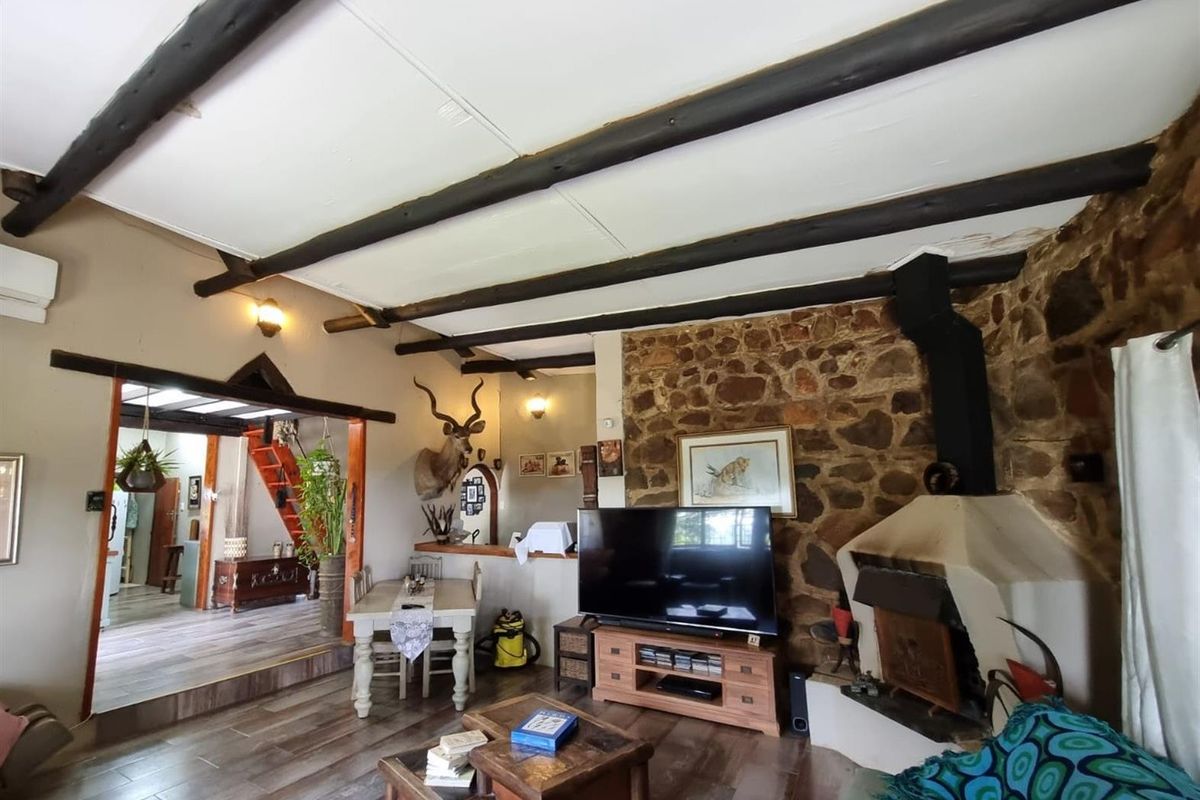 Rustic living area featuring exposed timber ceiling beams, a prominent natural stone feature wall, and a built-in fireplace.