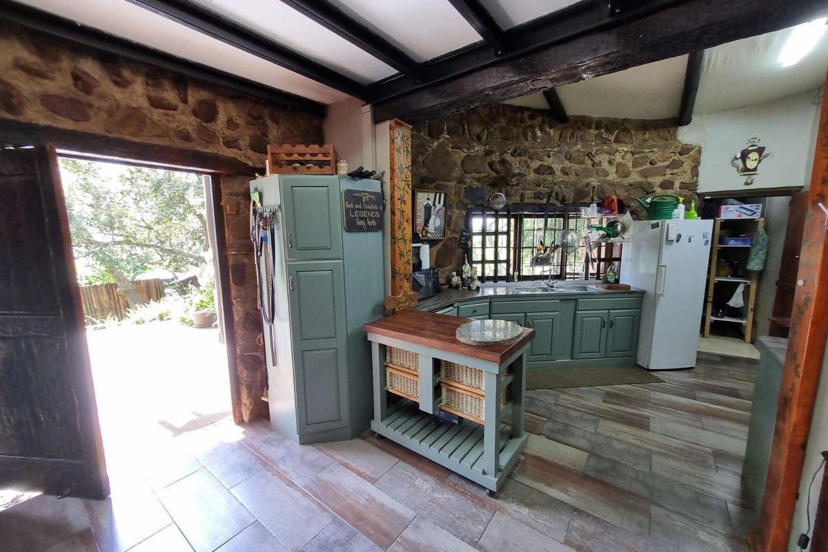 Rustic kitchen featuring exposed stone walls, timber ceiling beams, tiled flooring, and built-in cabinetry with direct access to an outdoor patio area.