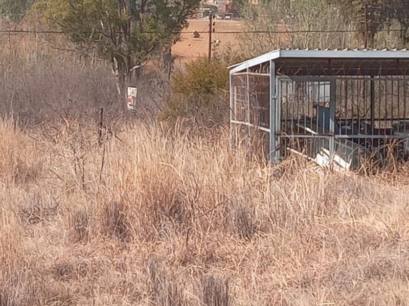 A view of a vacant residential plot featuring overgrown dry grass and a weathered metal storage structure.