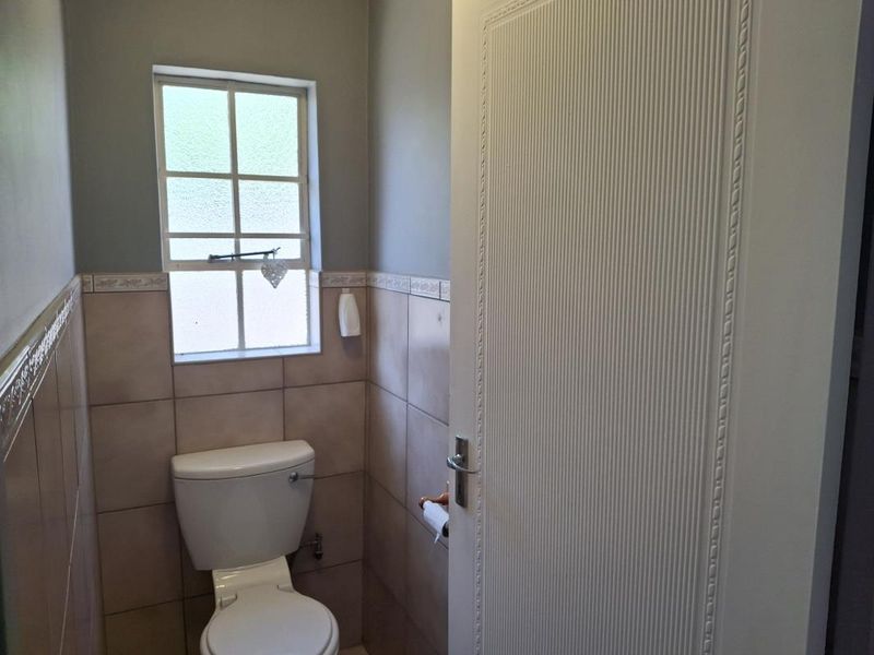 A compact guest bathroom featuring neutral wall tiles, a standard toilet, and a textured interior door.