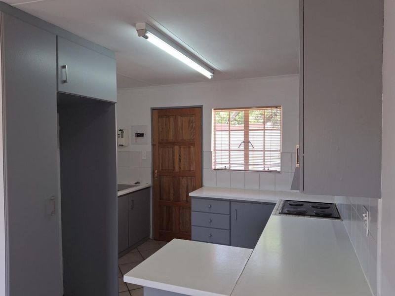 A functional kitchen featuring grey built-in cabinetry, white countertops, an integrated electric hob, and tiled flooring, offering a clean and practical workspace.