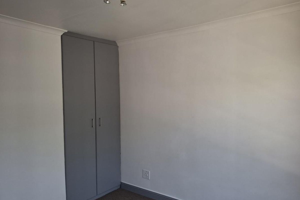 A clean, empty bedroom featuring neutral walls, carpeted flooring, and a built-in grey wardrobe.