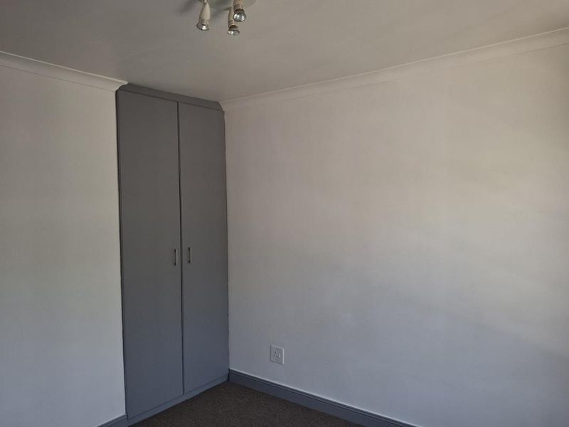 A clean, empty bedroom featuring neutral walls, carpeted flooring, and a built-in grey wardrobe.