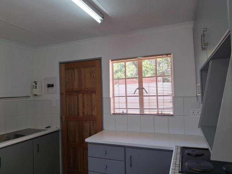 A functional kitchen featuring grey built-in cabinetry, white laminate countertops, a stainless steel sink, and an electric hob with tiled splashbacks.