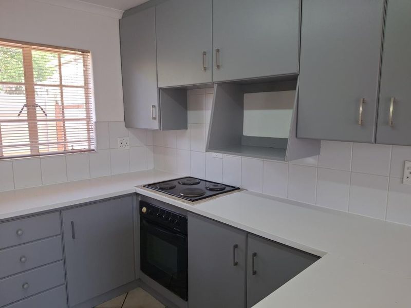 A clean, functional kitchen featuring grey built-in cabinetry, white tiled splashbacks, and integrated electric cooking appliances.