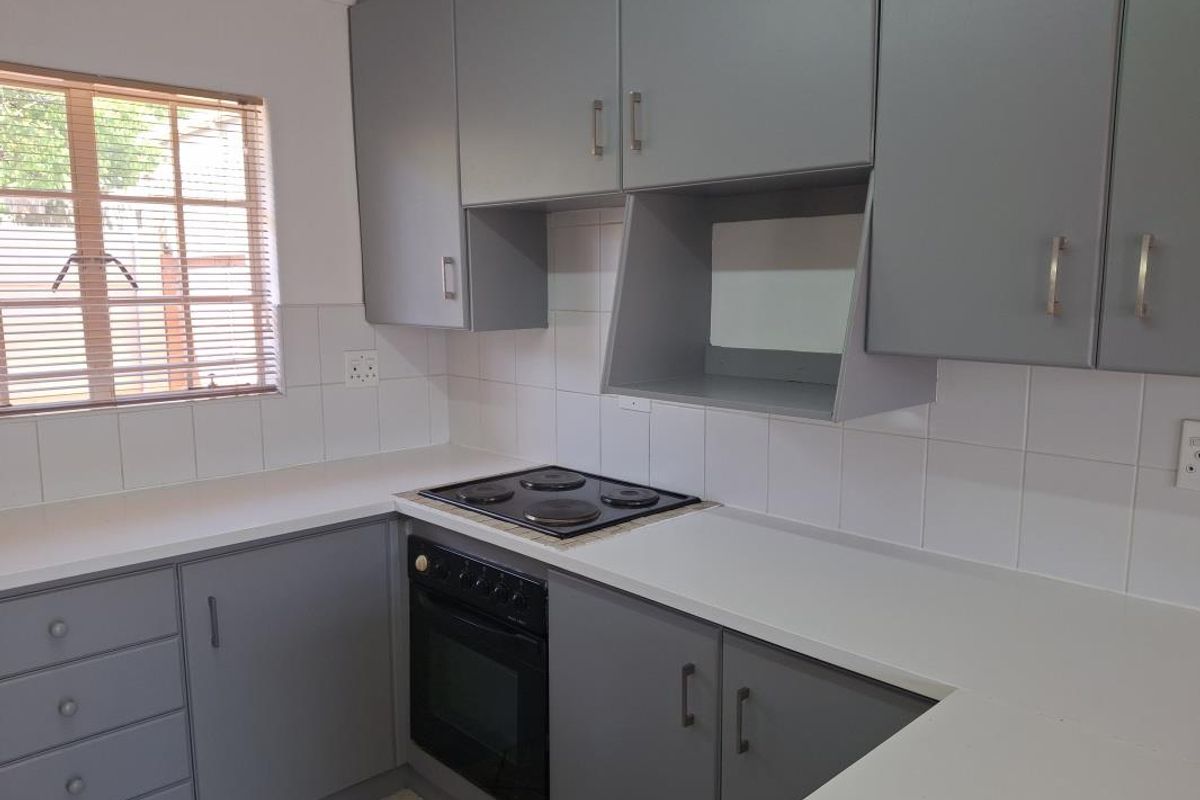 A clean, functional kitchen featuring grey built-in cabinetry, white tiled splashbacks, and integrated electric cooking appliances.