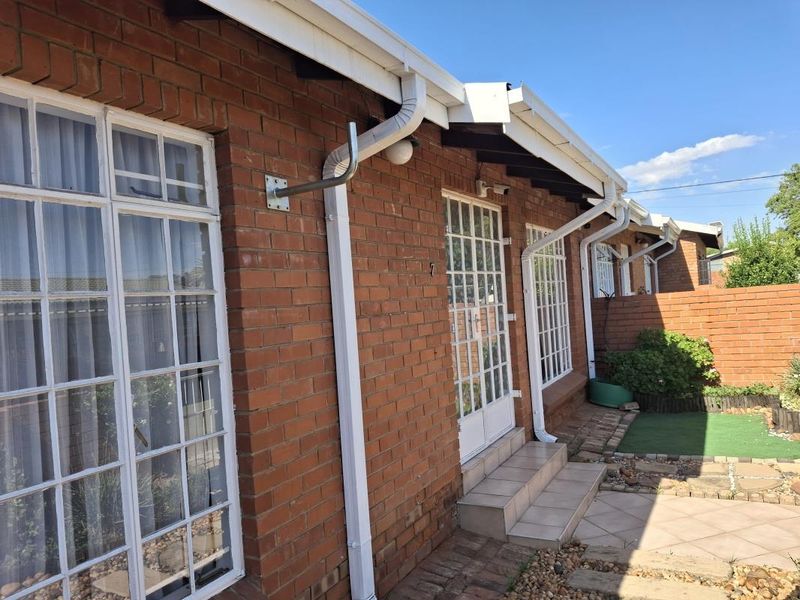 Rear exterior view of a townhouse featuring face brick walls, white aluminium window and door frames, and a small paved patio area.