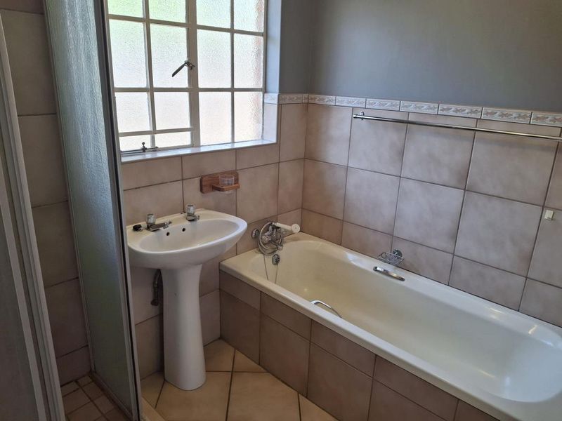A functional bathroom featuring a pedestal basin, a built-in bathtub, and a separate shower enclosure with neutral wall and floor tiling.
