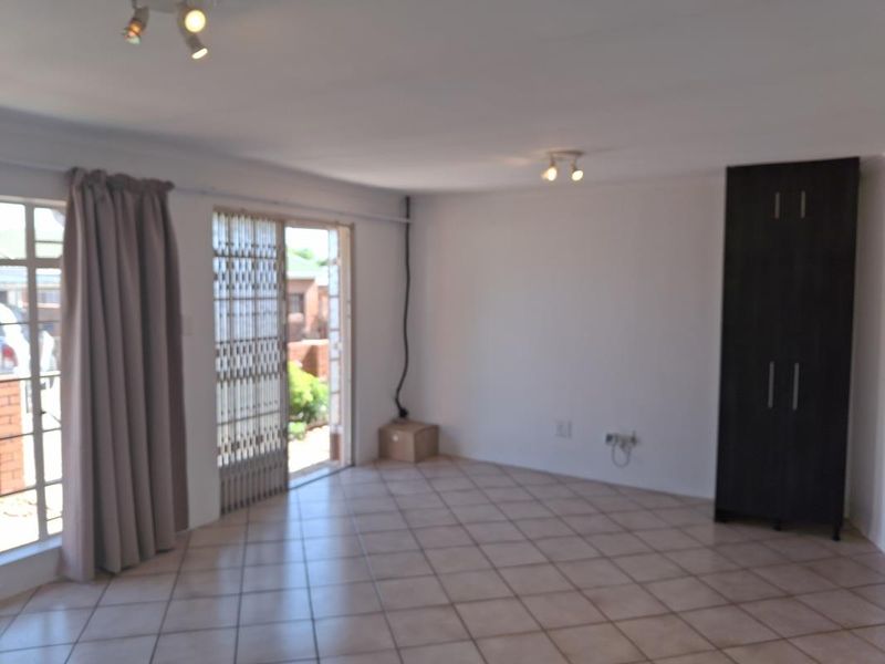 An open-plan living area featuring tiled flooring, a built-in cupboard, and a sliding door leading to the exterior, with visible electrical wiring.
