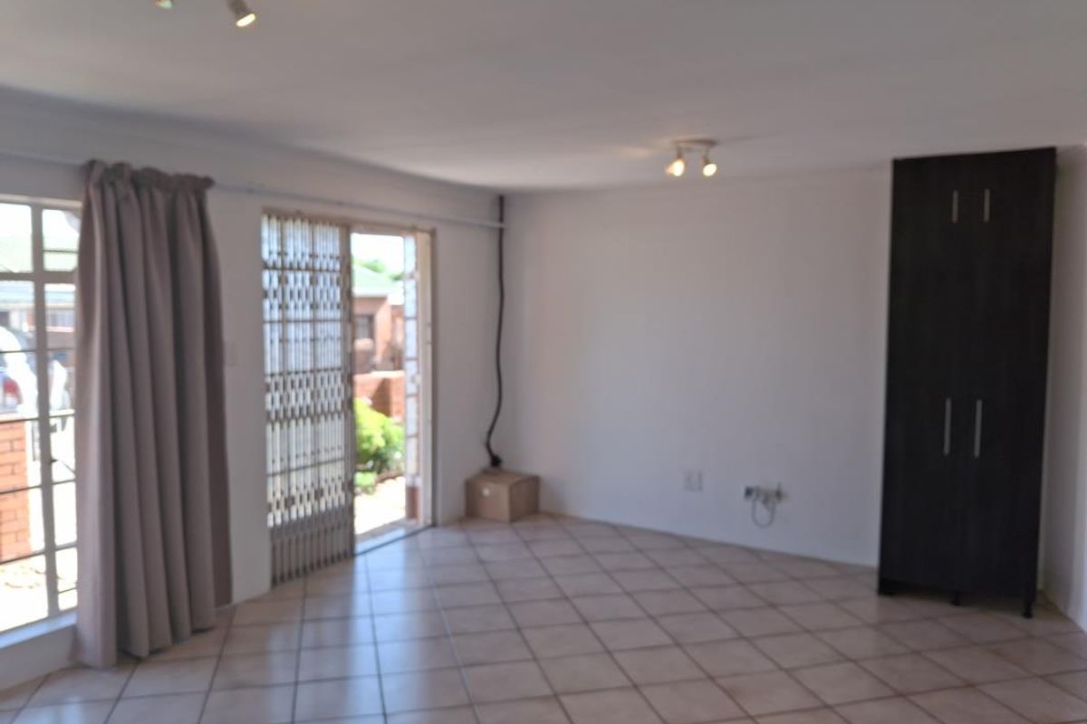 An open-plan living area featuring tiled flooring, a built-in cupboard, and a sliding door leading to the exterior, with visible electrical wiring.