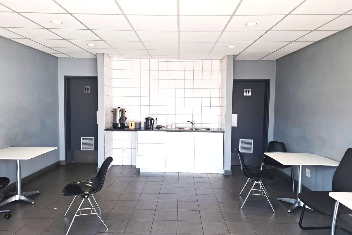 Commercial kitchenette area featuring tiled splashback, built-in cabinetry, sink, and adjacent restroom access points with tiled flooring throughout.