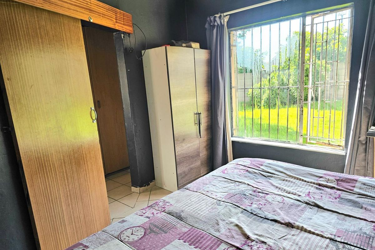 A bedroom featuring dark painted walls, a large window with security bars, and built-in wooden sliding door access to an adjacent space.