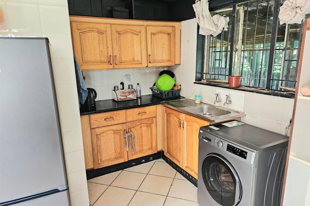 Compact kitchen featuring wooden cabinetry, tiled splashbacks, a stainless steel sink, and integrated space for a washing machine.