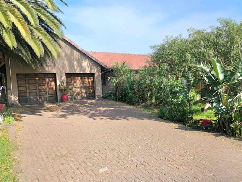 Front exterior view of the property featuring a paved driveway, double garage, and established garden landscaping.
