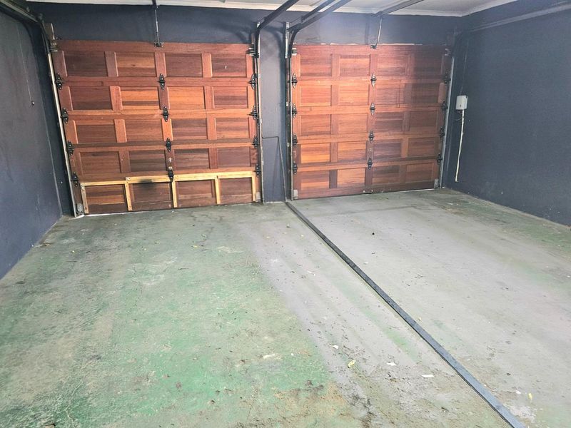 A double garage featuring two wooden sectional doors and painted concrete flooring, providing secure parking space.