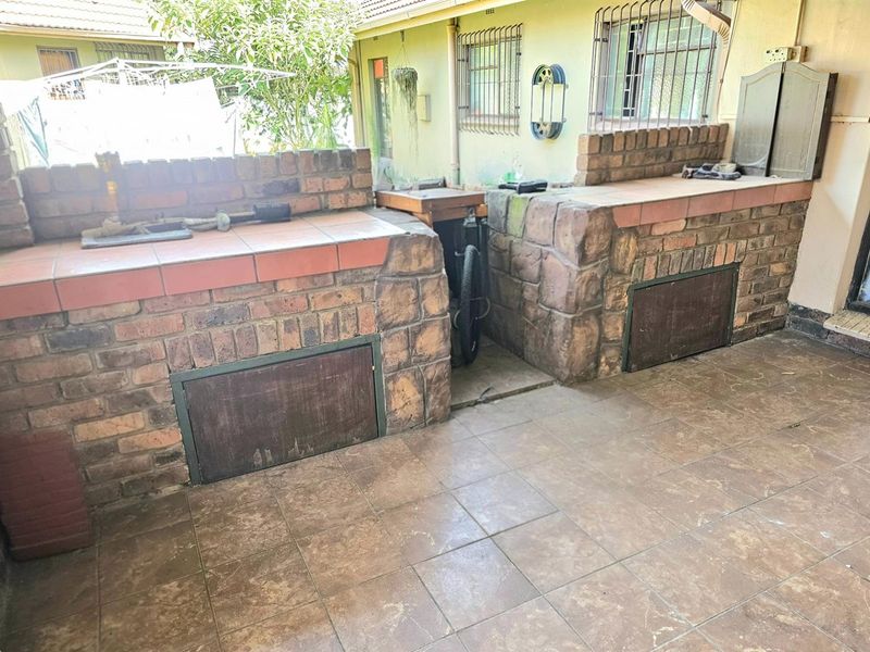 Outdoor patio area featuring a built-in brick braai or barbecue station with tiled countertops and storage access panels.