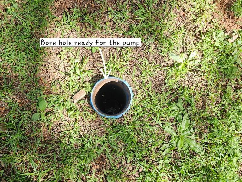 A view of an open borehole casing installed in the ground, prepared for the installation of a water pump system.