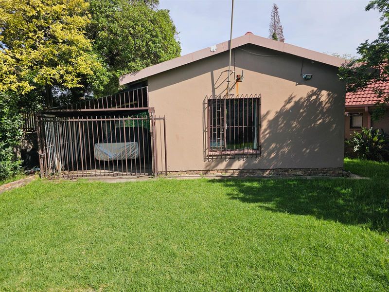 Rear view of the house featuring a lawn, a covered carport area with metal security gates, and a window with security bars.