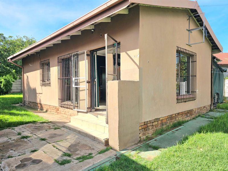 Rear exterior view of the house featuring a paved patio area, security bars on windows, and a small garden space.