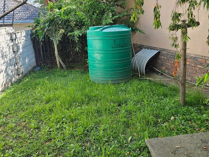 A rear garden area featuring a green water storage tank, brick boundary wall, and lawn space requiring maintenance.