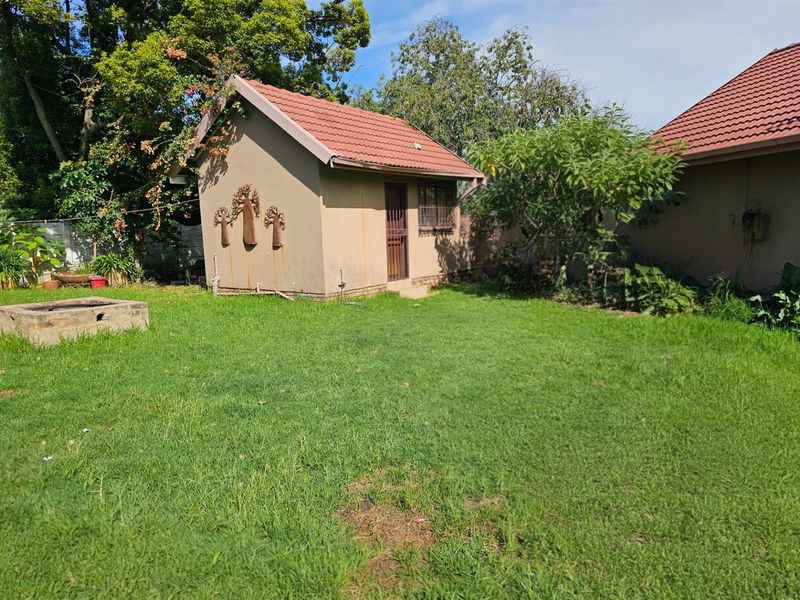 A view of the rear garden featuring a detached outbuilding with a tiled roof and a small brick fire pit area.