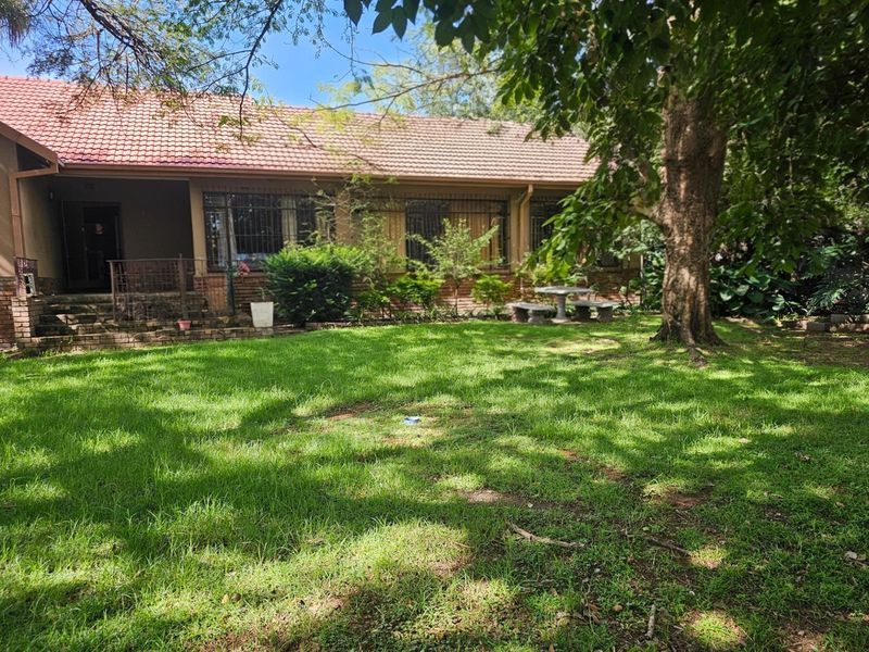 A view of the rear exterior of the house featuring a tiled roof, brick facade, and a spacious garden area with mature trees.