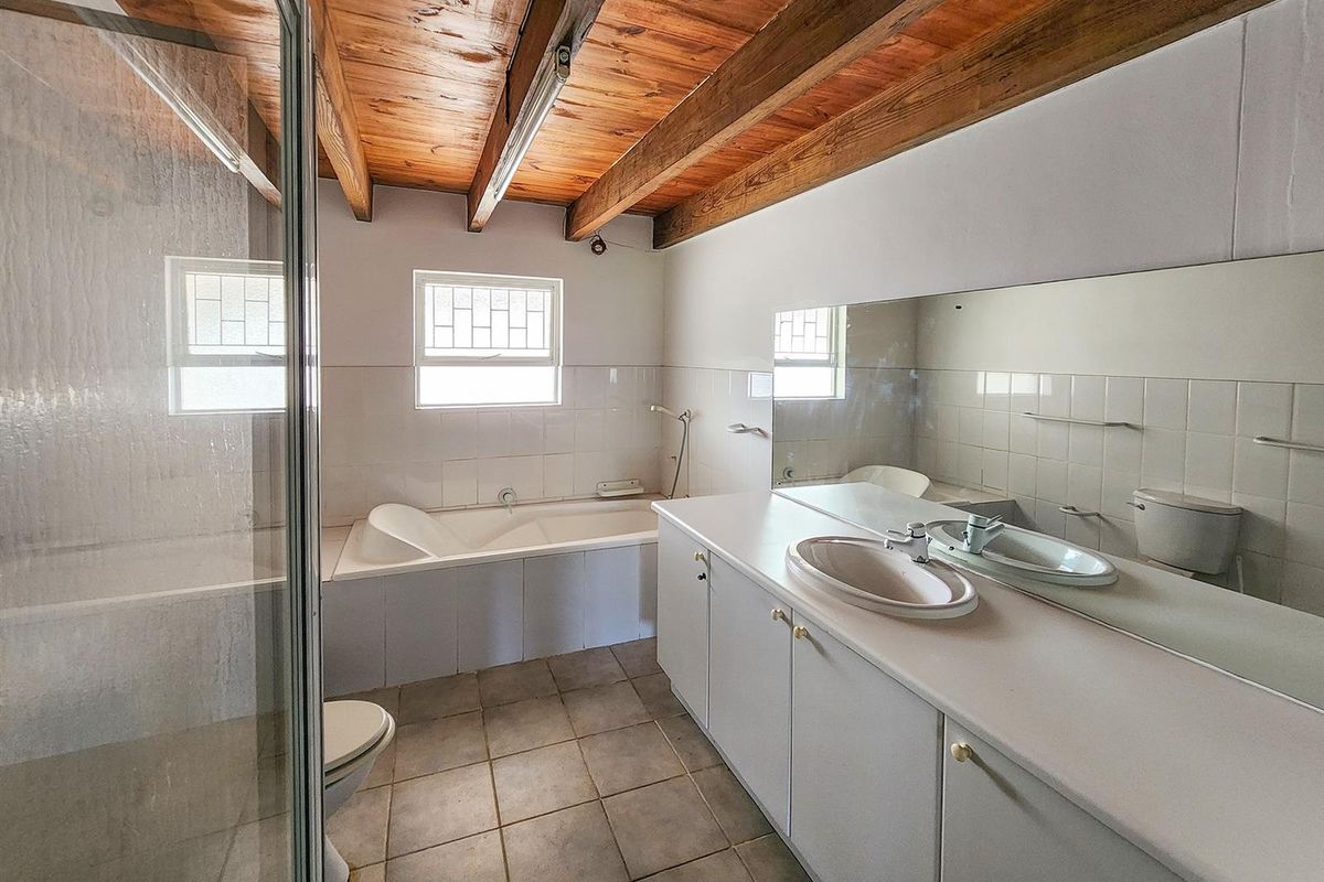 A functional bathroom featuring a built-in vanity with integrated basin, a separate shower enclosure, a bathtub, and exposed timber ceiling beams.
