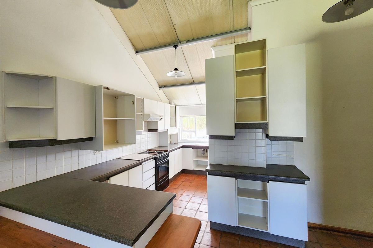 A dated kitchen featuring terracotta floor tiles, laminate countertops, and white cabinetry with several missing doors, set under a high vaulted ceiling.