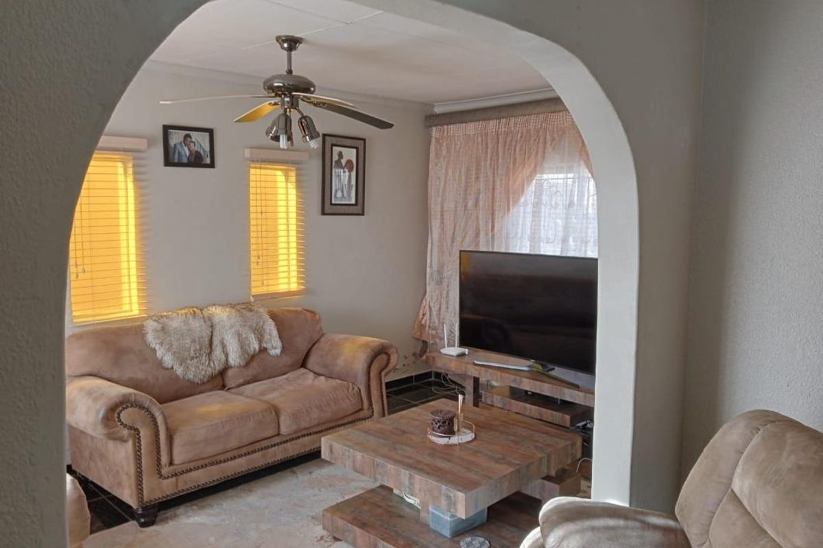 A living room featuring an arched entryway, ceiling fan, and tiled flooring, with visible wall finish wear near the baseboards.