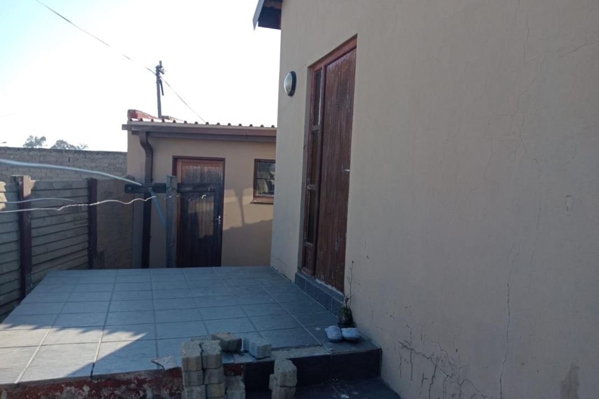 Rear exterior view showing a tiled patio area, timber door access, and visible plaster cracking on the building facade.
