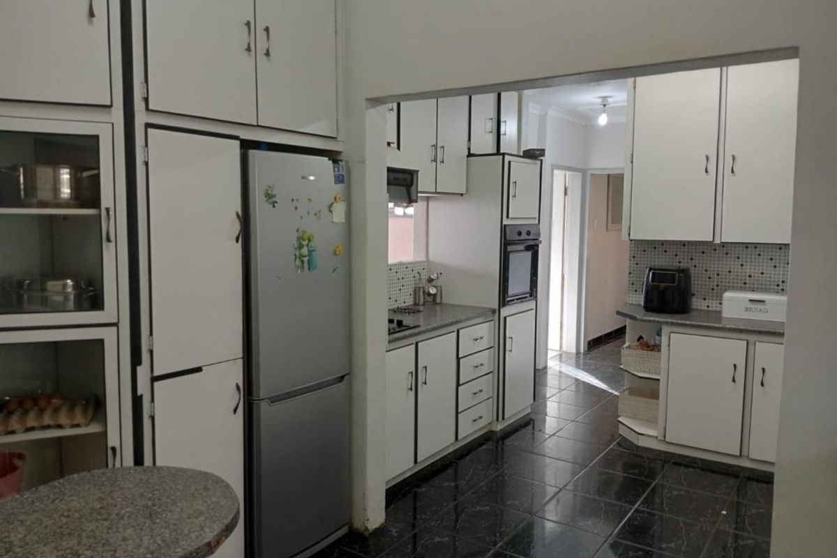 A dated kitchen featuring white built-in cabinetry, dark tiled flooring, and a mosaic backsplash, offering potential for a modern renovation.