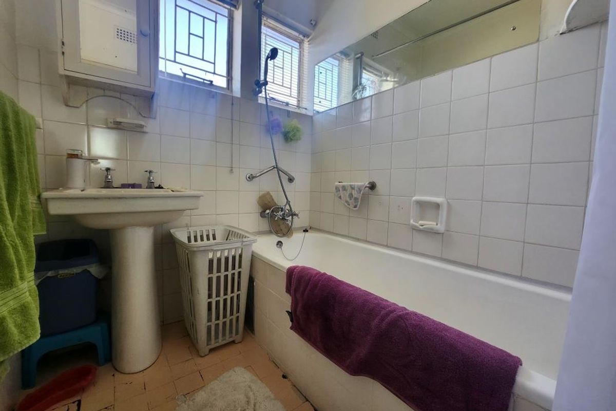 A dated bathroom featuring a pedestal basin, bathtub with shower mixer, and tiled finishes, offering potential for a modern renovation.