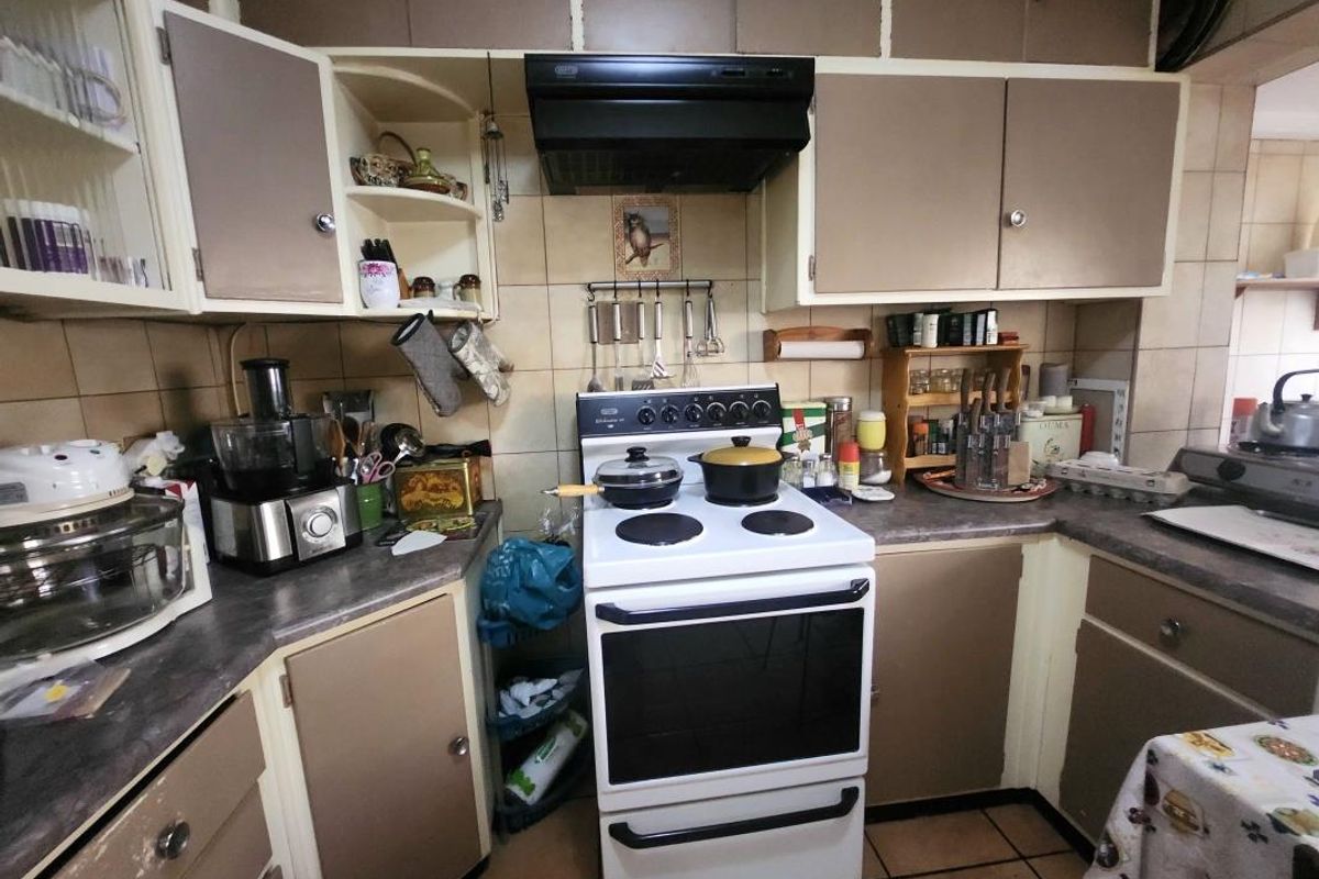 A compact kitchen featuring dated cabinetry, laminate countertops, a tiled backsplash, and a freestanding stove with an extractor fan.