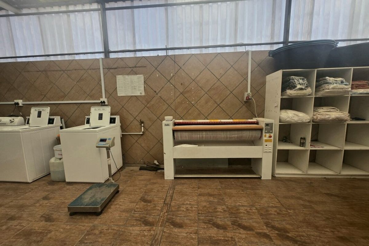 Functional laundry area featuring tiled flooring, wall cladding, and built-in shelving, suitable for commercial washing and ironing operations.