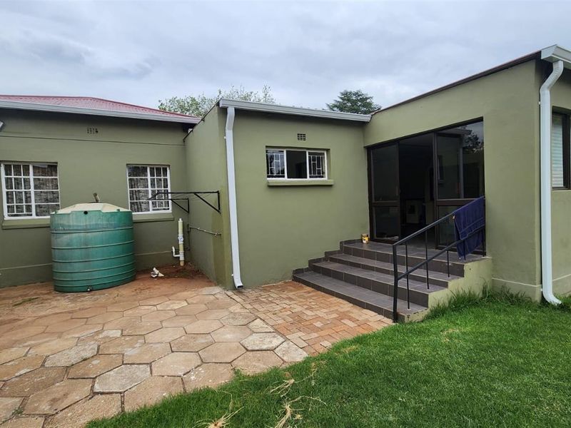 Rear exterior view of the house featuring a paved patio area, a water storage tank, and a set of steps leading to the entrance.