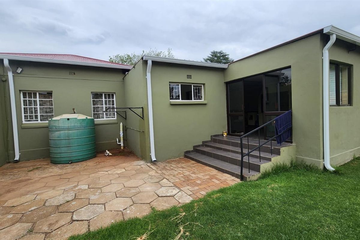 Rear exterior view of the house featuring a paved patio area, a water storage tank, and a set of steps leading to the entrance.
