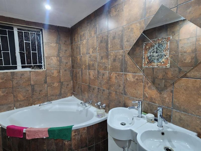 A bathroom featuring a corner bathtub, double vanity basins, and full-height brown ceramic wall tiling with a decorative accent feature.