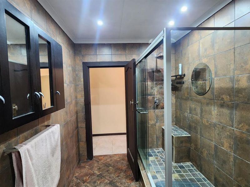 A bathroom featuring a glass-enclosed shower with a built-in bench, dark cabinetry, and full-height wall tiling.