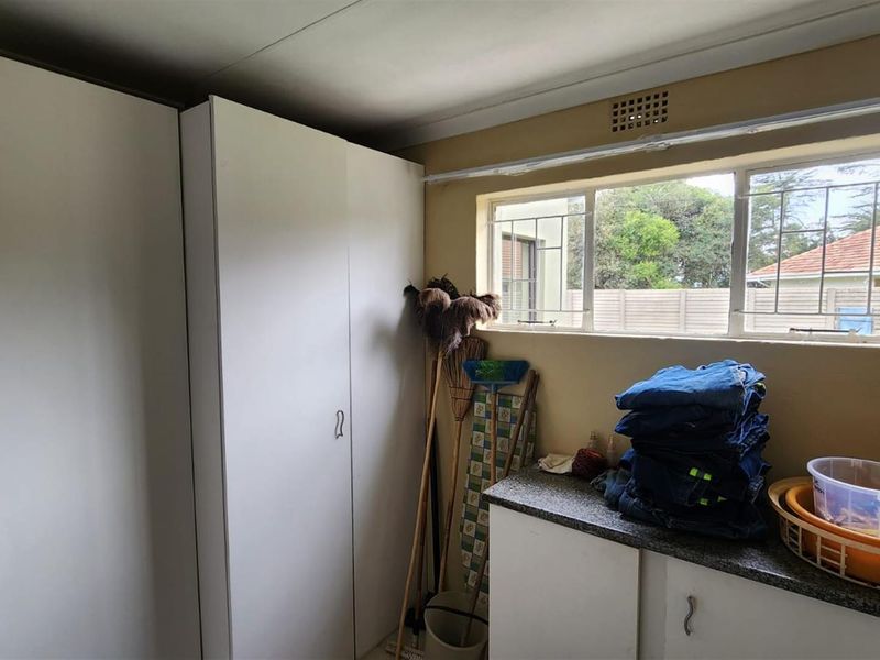 A functional laundry room featuring built-in white cabinetry, a stone-look countertop, and a window with security bars.