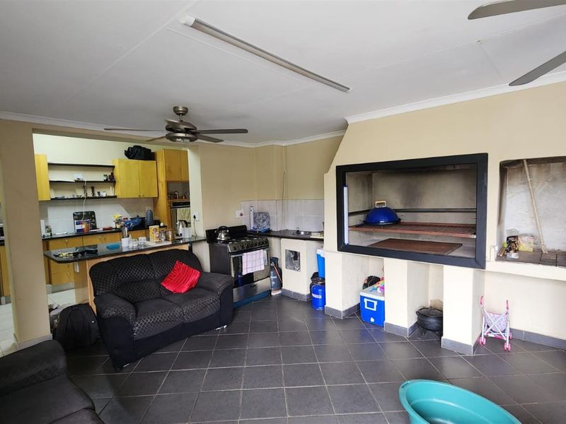 Open-plan living area featuring a built-in indoor braai, tiled flooring, and an adjoining kitchen with wooden cabinetry.