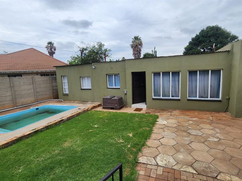 Rear view of the property featuring a swimming pool, paved patio area, and a small garden space with direct access to the home.