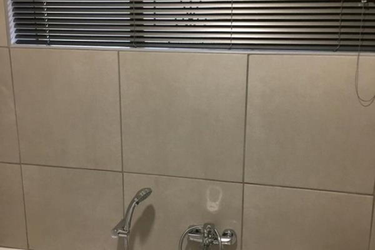 A clean bathroom featuring a built-in bathtub with chrome fixtures and neutral wall tiling, complemented by functional venetian blinds.