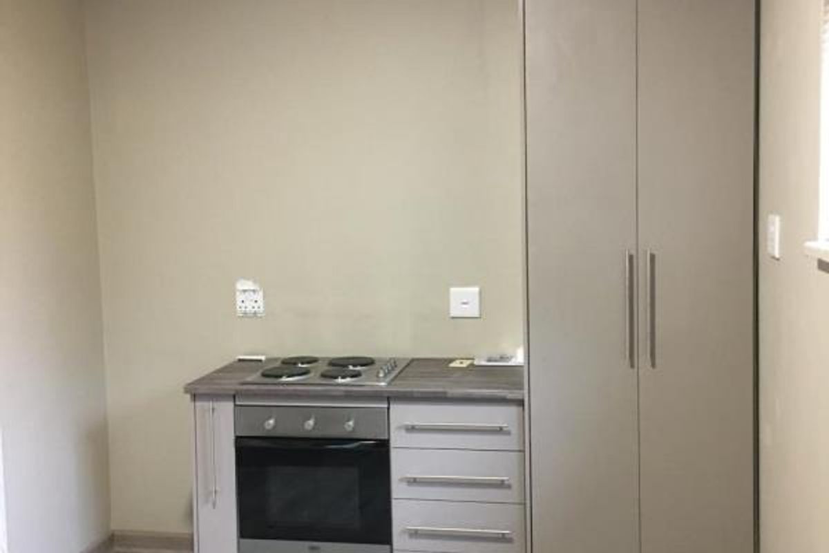 A compact kitchen area featuring modern laminate flooring, built-in cabinetry, a fitted oven and hob, and a tall pantry cupboard.