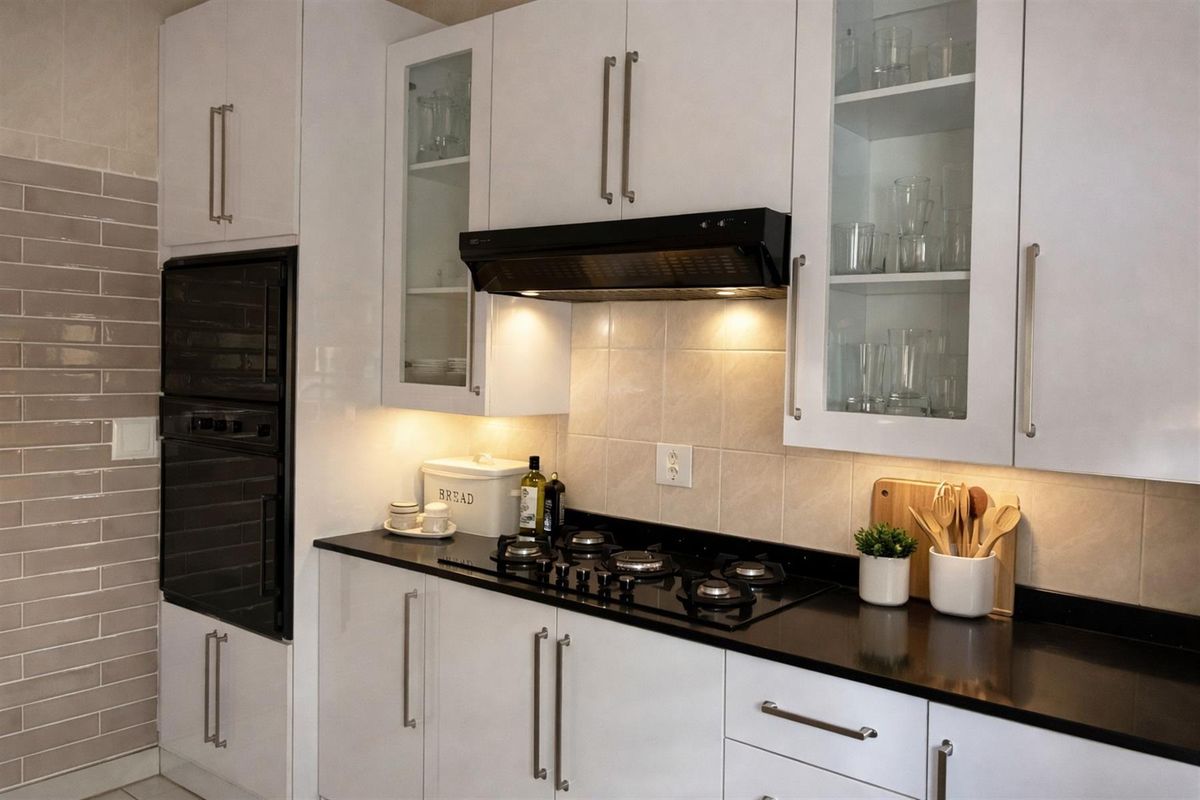 Modern kitchen featuring high-gloss white cabinetry, black stone countertops, a built-in oven, and a gas hob with an integrated extractor fan.